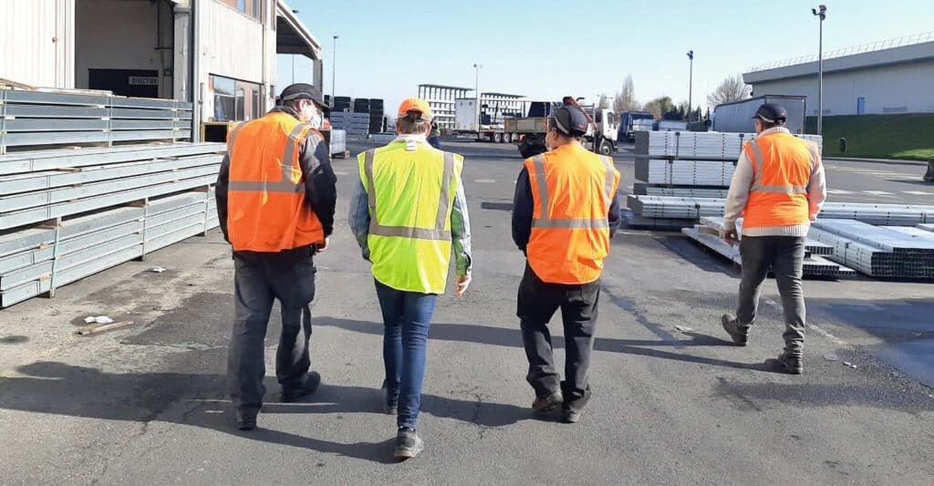 4 personnes vêtues de gilets jaunes et oranges et portant des casques de sécurité, marchent sur l'un des sites industriels du Groupe Knauf.