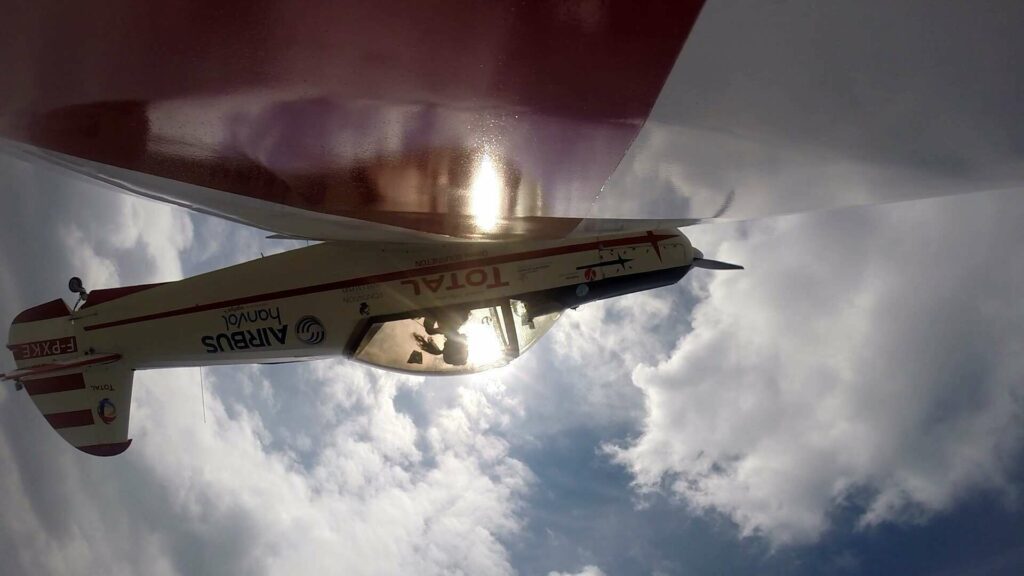 Image d'un petit avion à l'envers en train de voler, la caméra se trouve au bout d'une aile, permettant ainsi de voir l'intérieur de la cabine. La pilote de l'aerodyne est Dorine Bourneton, première femme handicapée à réaliser de la voltige aérienne.