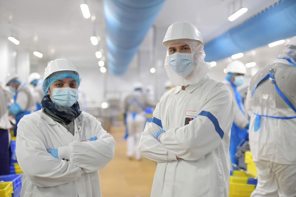 2 collaborateurs d'Elivia, en tenue règlementaire prennent la pose. Tout deux portent une blouse, des gants, une charlotte, un casque de sécurité ainsi qu'un masque.